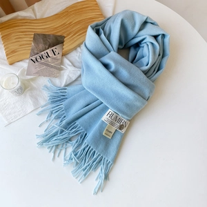 Détail d'une écharpe bleu clair en imitation cachemire avec franges et étiquette de marque