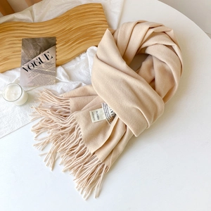 Détail d'une écharpe en faux cachemire crème avec franges denses et étiquette de marque