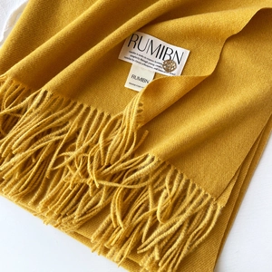 Détail d'une écharpe en cachemire jaune moutarde avec bord à franges et logo en métal doré
