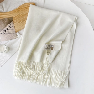 Détail d'une écharpe en cachemire blanc cassé avec franges et étiquette sur une table