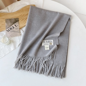 Détail d'une écharpe gris clair style cachemire avec franges et étiquette sur plateau bois