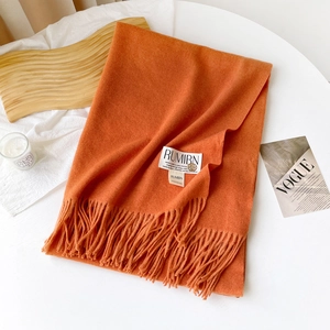 Détail d'une écharpe orange douce avec franges et étiquette sur plateau décoratif