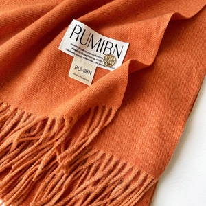 Détail d'une écharpe orange toucher cachemire avec pendentif logo doré et franges douces