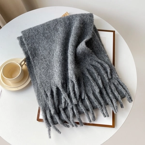 Close-up of thick dark grey knitted scarf with long tassels on a cozy wooden tray