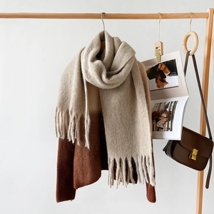 Detail of light beige knit scarf with long tassels draped on a wooden hanger