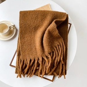 Caramel brown knit scarf with fringe tassels on white table in warm minimalist setting