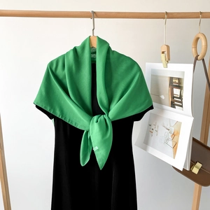 Detail eines leuchtend grünen Seidenschals, an einem schwarzen Kleid elegant gebunden