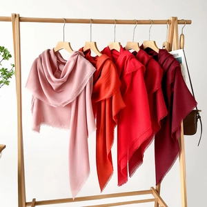 Macro detail of red gradient pashmina scarves with delicate fringed edges on wood hanger