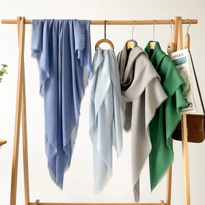 Detail view of solid color scarves with fringed edges hanging on a wooden hanger