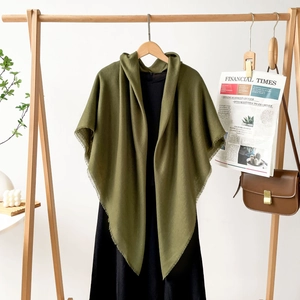 Detail of olive green shawl with fringe edges on a wooden hanger with black dress