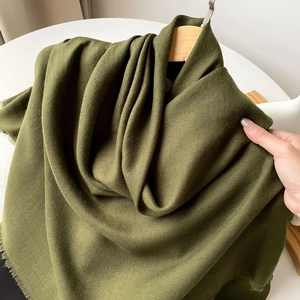 Close-up of a dark green shawl with fine tassel edges and soft cotton-linen texture