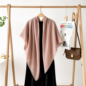 Detail of soft dusty pink pashmina shawl with tassel trim styled on a wooden hanger
