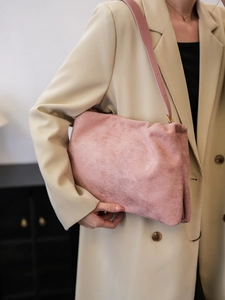 Close-up of pink suede cloud bag with soft pleats and thin strap on model shoulder