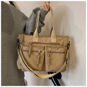 Detail of khaki nylon tote bag with three zip pockets and woven tassel pulls for daily use