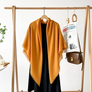 Close-up of ginger yellow tassel shawl on a wooden hanger with a black dress