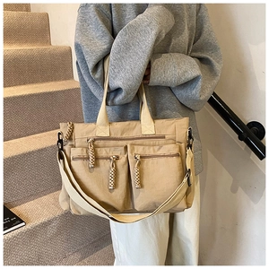 Detail of khaki nylon tote bag showing multi-zipper pockets and woven rope pullers