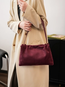 Detailed view of burgundy suede handbag worn over a cream coat for daily commute