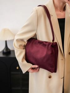 Close-up of burgundy velvet Boston bag with golden buckle on a beige suit model