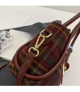 Détail macro du fermoir doré sur un sac cabas en laine à carreaux et garniture brune