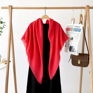 Detail of red oversized scarf with delicate fringe edges on a wood hanger