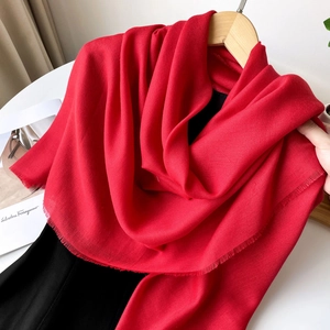 Detail of red square scarf with fringe edge on wooden hanger showing soft fabric texture