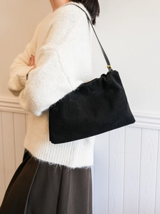 Detail of a black suede Boston bag showing soft pleats and elegant gold hardware