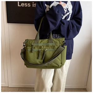 Detail of army green multi-pocket nylon tote showing shoulder strap and zipper compartments