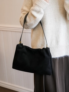 Close-up of black suede Boston shoulder bag with gold buckles worn over a knit sweater