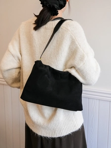 Side view of black suede shoulder bag with golden rings worn on beige knit sweater