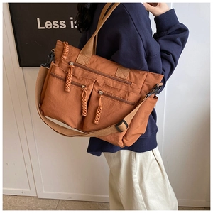 Close-up of rust-red multi-pocket tote bag with wide canvas straps and woven zipper pulls