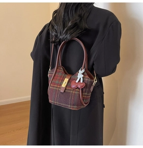 Détail du sac cabas en laine à carreaux avec bordure en cuir et pendentif cerise