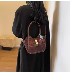 Détail du sac cabas en laine quadrillée avec poignée en cuir et breloque cerise sur manteau