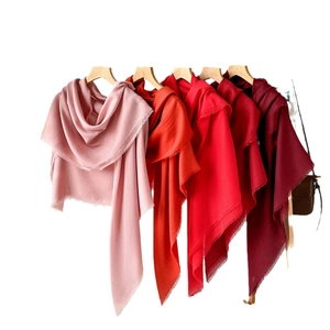 Solid color scarves for women in various shades with fringe details on wooden hangers
