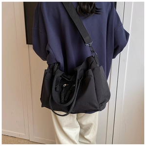 Detail of a black multi-pocket tote bag with woven zipper pulls and nylon material