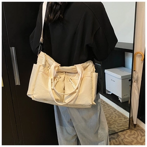 Detail view of beige multi-pocket tote bag with woven zipper pulls and wide strap