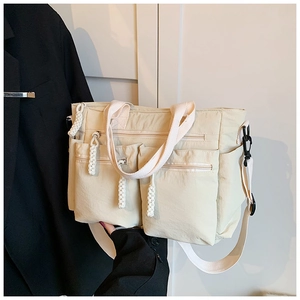 Detail of beige multi-pocket tote bag showing reinforced handles and nylon texture