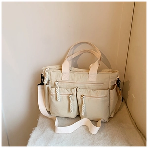 Close-up of cream nylon tote bag with multi-pocket details and woven rope zipper pulls