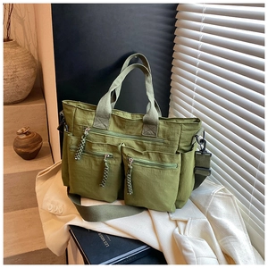 Detail of green multi-pocket tote bag with woven zipper pulls on minimalist background