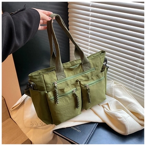 Detail of army green multi-pocket nylon tote bag resting on a white suit with a book