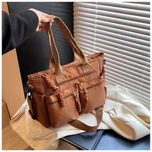 Detail of a brown nylon multi-pocket tote bag with weave-cord zippers and a wide strap