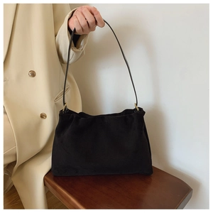 Detail of black suede Boston bag on vintage wooden stool with long shoulder strap