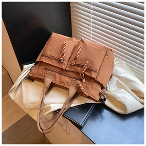 Detail of a brown multi-pocket nylon tote bag with woven zipper pulls and long shoulder strap