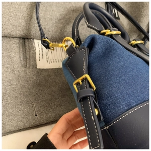 Detailed close-up of dark blue denim and leather stitching with gold buckles on bag