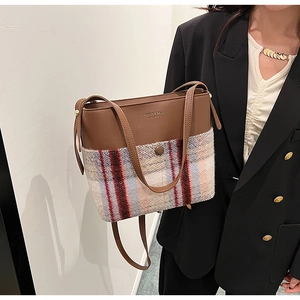 Détail d'un sac seau en cuir marron et laine à carreaux porté sur l'épaule
