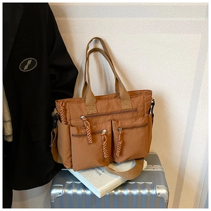 Detail of caramel nylon tote bag with multi-zip pockets on a silver suitcase