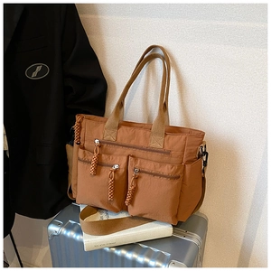 Detail of brown multi-pocket tote bag with woven zipper pulls and nylon strap