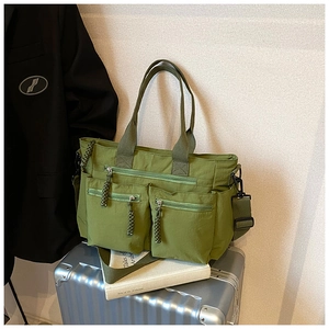 Detail of army green multi-pocket nylon tote bag with braided zipper pulls on a suitcase