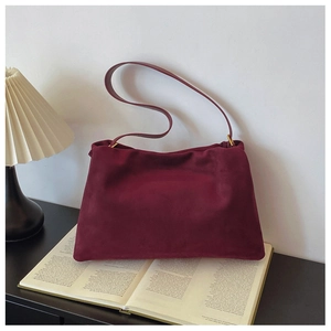 Detail shot of burgundy suede Boston bag placed on a book with vintage lamp lighting