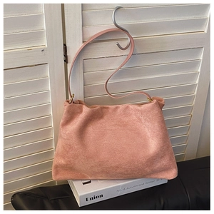 Detail of soft pink matte faux suede Boston shoulder bag hanging on a hook in soft lighting