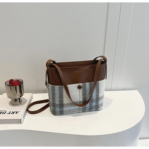 Détail de la couture en cuir marron et laine à carreaux bleue sur le sac fourre-tout